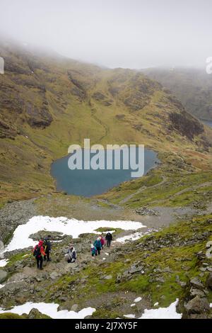 Walkers ascending the path up the north east flank of The Old Man of Coniston above Low Water in late winter the Lake District National Park, Cumbria, England. Stock Photo