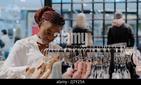 Portrait serious focused young girl shopper female consumer runs across rack african american woman choosing clothes in shopping center buying Stock Photo