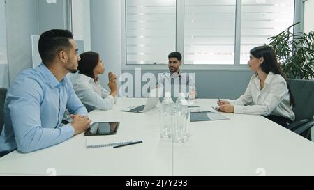 Business people sitting at conference table. Confident arabic businessman talking to colleagues or partners, male leader discussing work at meeting or Stock Photo