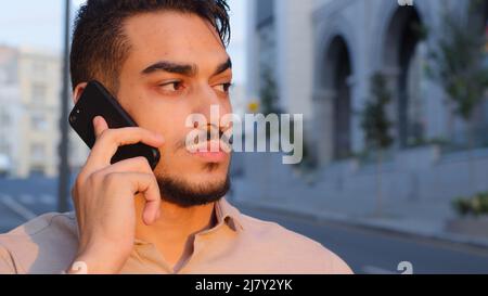 Close-up hispanic emotional business man bearded serious guy talking on mobile phone answering call using smartphone remote talk cellular connection Stock Photo