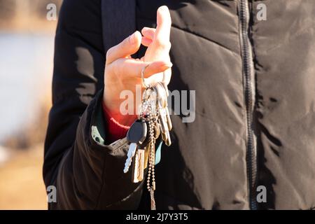the girl holds in her hands the keys to the apartment on the street in the sun, the keys to the house, buying and renting real estate Stock Photo