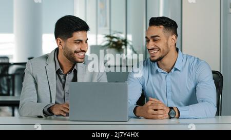 Cheerful smiling male colleagues employees cooperating in office talking working together at workplace, optimistic businessmen coworkers discussing Stock Photo