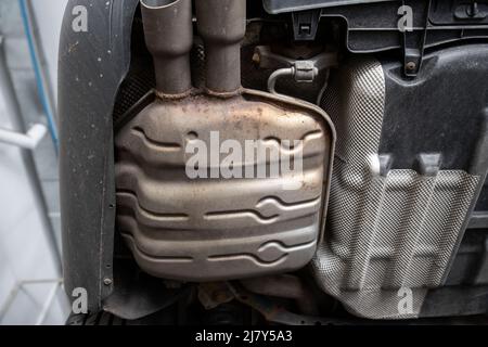 Close-up detail bottom view of car part metal exhaust muffler pipe with rusty stains. Lifted vehicle check-up maintenace service, repair and fix at Stock Photo