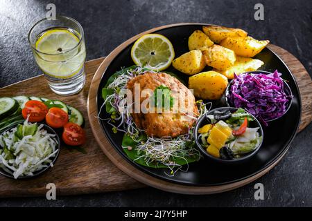 Pulled chicken cutlet coated with breadcrumbs with potatoes and vegetable salads Stock Photo
