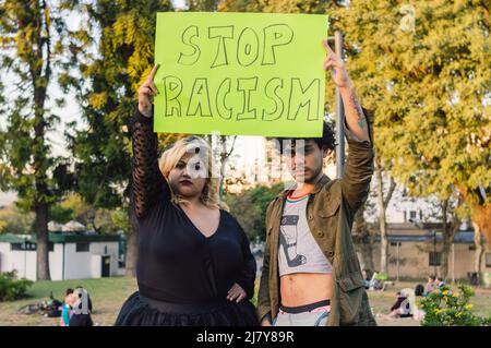 young plus size woman and homosexual man, outdoors in a public park, protesting holding a sign that says 'stop racism' Stock Photo