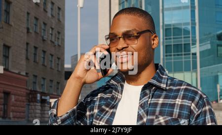Stylish happy african man wearing trendy sunglasses speaks mobile phone in city. Close-up male dark-skinned face talking smartphone. Portrait of Stock Photo