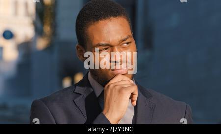 Pensive millennial black student considering choice makes difficult decision outdoors, confident serious african american young adult businessman Stock Photo