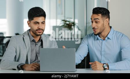 Indian oriental millennial male businessmen looking at laptop screen discussing project, satisfied with result of negotiations Arab colleagues working Stock Photo