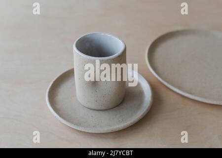 a beige ceramic cup and plates on a wooden table top view. minimalist set of handmade ceramic tableware and pottery Stock Photo