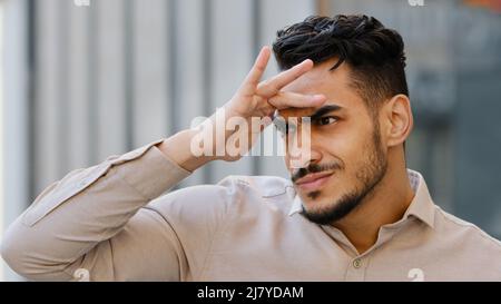 Close-up male suspicious face portrait outdoors in city spy bearded guy funny man looking into distance searching holding hands near forehead peeking Stock Photo