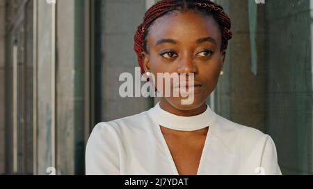 Close-up female portrait african american girl lady woman student businessperson face stylish model stands in city on building background looking into Stock Photo