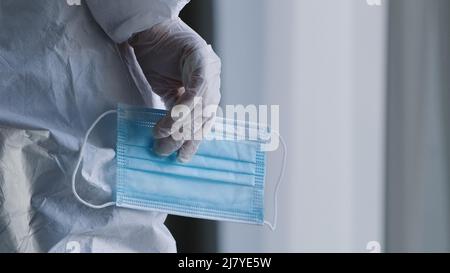 Close-up unrecognizable doctor unknown nurse surgeon practitioner in white uniform protective suit in latex medical gloves holds transparent glasses Stock Photo