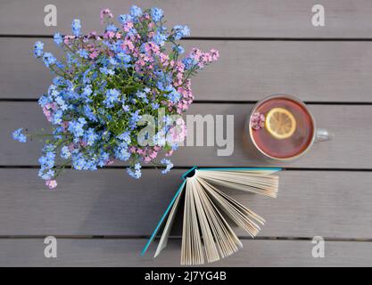 Still life with cup of tea on table, an open book and forget-me-not flowers. Nice morning picture. Time for rest and tea drinking. Reading book with p Stock Photo