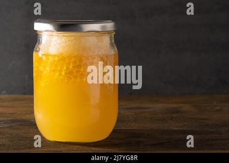 Jar of honey with honeycombs. Yellow transparent bee product. Half liter packaging with space for a label. Wooden background. Bee honey in a glass jar. Natural healthy food. Copy space. Stock Photo