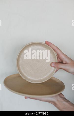 Hands holding ceramic plates isolated on white background. Minimalist set of handmade ceramic tableware and pottery Stock Photo