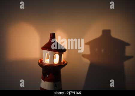 burning candle in a candlestick in the shape of a lighthouse with a shadow, cozy warm atmosphere Stock Photo