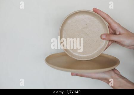 Hands holding ceramic plates isolated on white background. Minimalist set of handmade ceramic tableware and pottery Stock Photo
