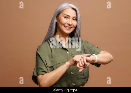 Mature beautiful asian woman with grey hair wearing casual clothes In hurry pointing to watch time, impatience, talking about deadline delay Stock Photo