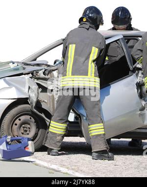 two firefighters as they remove the door of a car crashed after the road accident on the highway Stock Photo