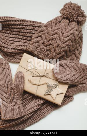 Knitted hat, scarf and mittens and a Christmas gift wrapped in paper on a white background Stock Photo