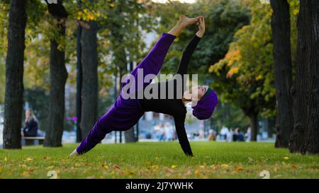 Strong sportive islamic girl in hijab yoga teacher woman stands in side plank on grass in park doing Ardhachandrasana Vasishthasana asana pose Stock Photo