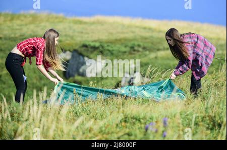 Temporary housing. Camping trip. Helpful to have partner for raising tent. Camping skills concept. In middle of nowhere. Girls set up tent on top of Stock Photo