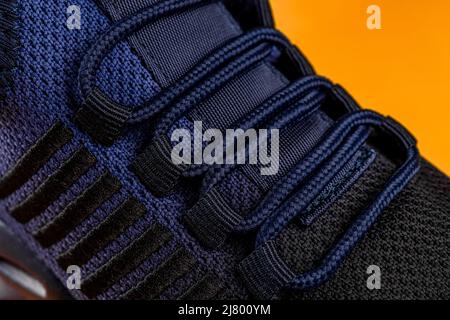 Laced up fastening of new sport shoe against orange background. Lacing of black blue mesh fabric sneakers macro. Textile sneakers with elastic laces. Stock Photo