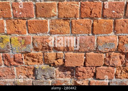 Red brick pattern. An old brick wall with cracks and scratches. A wall with the texture of broken bricks. Vintage facade of the house. Stock Photo