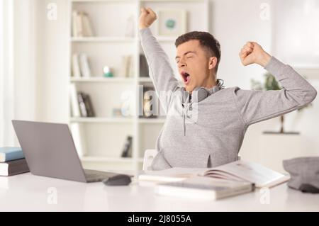 Male student yawning during online class in front of a laptop computer at home Stock Photo