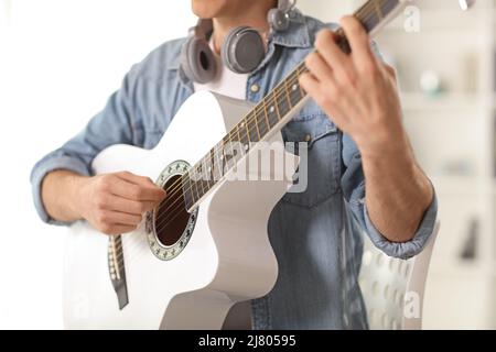 Crop shot of a young man playing a white acoustic guitar seated in a chair Stock Photo