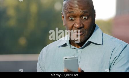 Worried nervous african man holding cell phone frustrated by problem having complaints on bad service, angry black person annoyed with mobile app Stock Photo