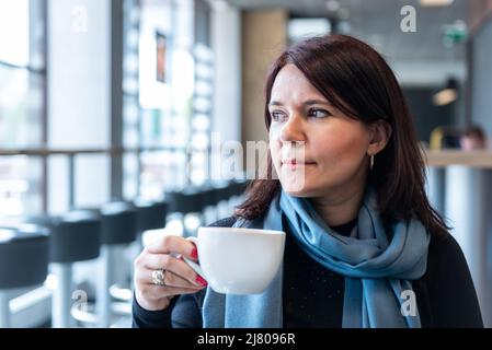 Thoughtful mature woman sitting in cafeteria holding coffee mug. Middle aged woman drinking tea while thinking. Relaxing and thinking while drinking c Stock Photo