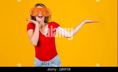 Excited girl holds something on open palm. Season sale and discount. Funny woman in big glasses. Stock Photo