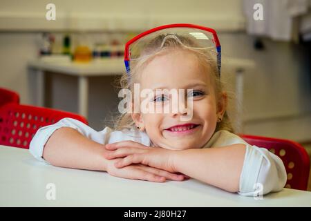 clever blonde school girl chemist in eyeglasses and white medical gown making science experiments chemistry ,mixing different chemical solutions in Stock Photo