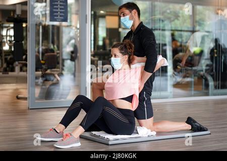 Personal trainer in the gym helping a client do stretching exercises while using face masks during the Covid-19 epidemic Stock Photo