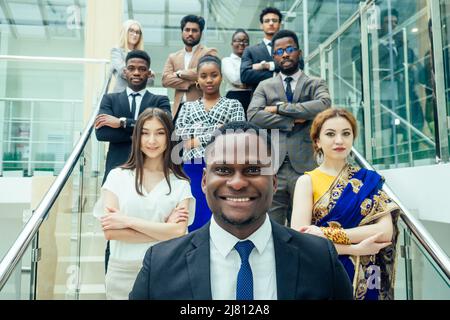 Multi Nationality of business people : indian, korean, afro-american and caucasian stand on the stairs in a modern office with panoramic windows Stock Photo