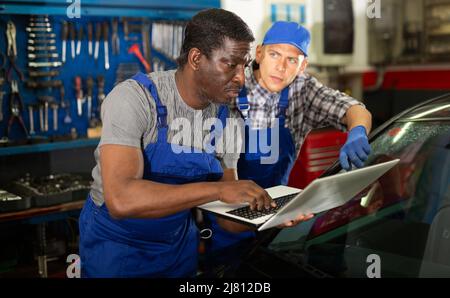 Two auto mechanics diagnosing car engine with laptop Stock Photo