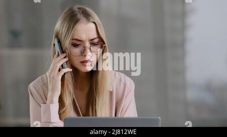 Angry caucasian woman call phone at office work place annoyed girl talking mobile conversation upset mad female worker boss leader cellphone argue Stock Photo