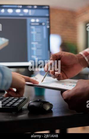 Close up of 3D digital artists reviewing sketch scene plan and simulated render times, Creative industry enthusiasts with CAD open in background discussing technical issues while pointing at clipboard Stock Photo