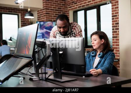 African american company coworker standing near production department team leader desk while discussing. Digital graphic artist with colleague talking about future of project. Stock Photo
