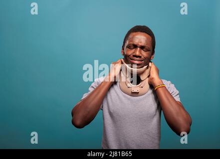 Emotional guy wearing cervical collar to cure physical injury after sprained bone accident. Young man with neck foam suffering from fractured vertebrae, being in pain at rehabilitation. Stock Photo