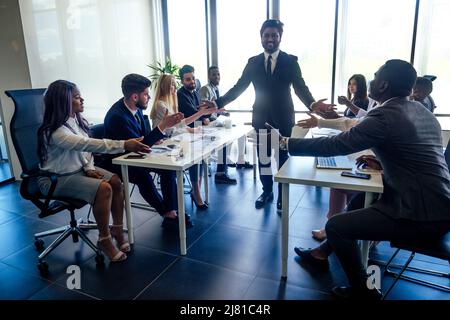 creative team of multiracial men sitting round the desk in formal clothes talking over new project in meeting room Stock Photo