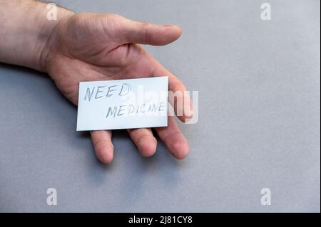Need medicine. Handwritten gray lettering. Open man's palm with white business card against gray background. Concept of helping people in need. Volunt Stock Photo