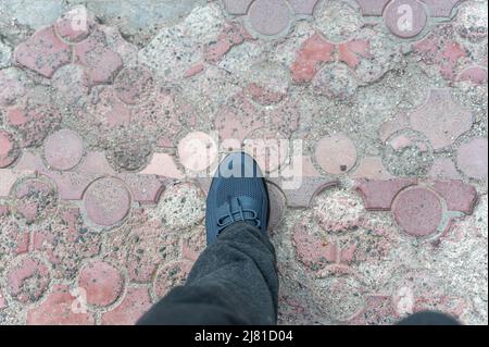 A view of my feet walking on the old paving stones. A mature man in gray pants and blue sneakers walks down the steps. Outdoors.  Daytime. Selective f Stock Photo