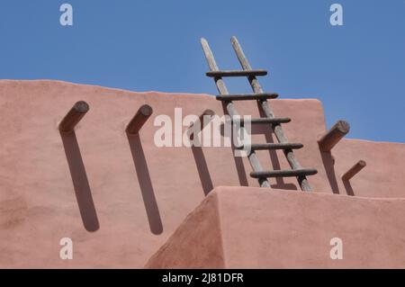 Adobe roof detail with wooden ladder and wooden posts against blue sky Stock Photo