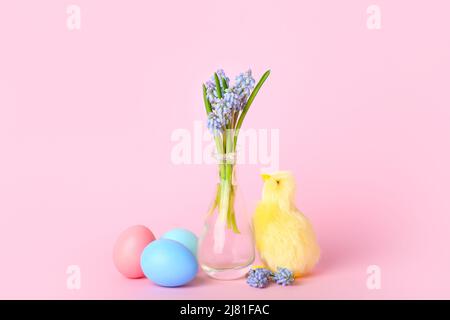 Cute yellow chicken, vase with flowers and Easter eggs on pink background Stock Photo