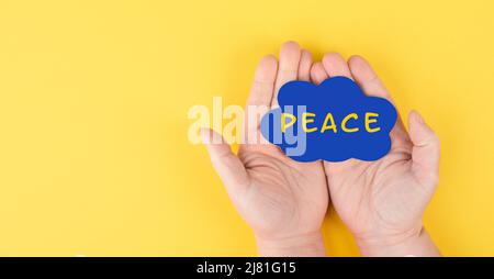 Holding a cloud with the word peace in the hands, stop war, support Ukraine, living peaceful together, color of ukrainian flag Stock Photo