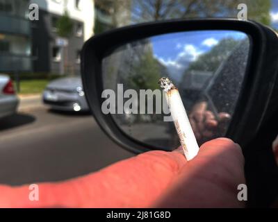 Berlin, Germany. 27th Apr, 2022. A person smokes a cigarette while driving. Credit: Paul Zinken/dpa/Alamy Live News Stock Photo
