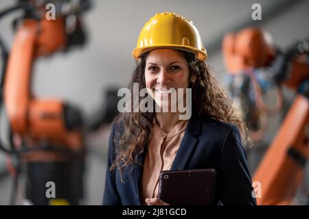 Automation female engineer with tablet for programming robotic arm in factory. Stock Photo