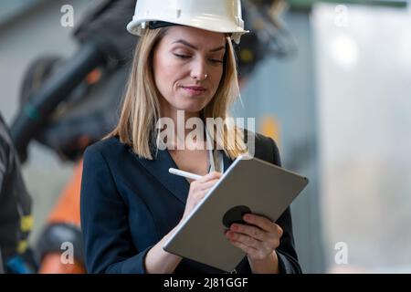Portrait of female chief engineer in modern industrial factory using tablet. Stock Photo